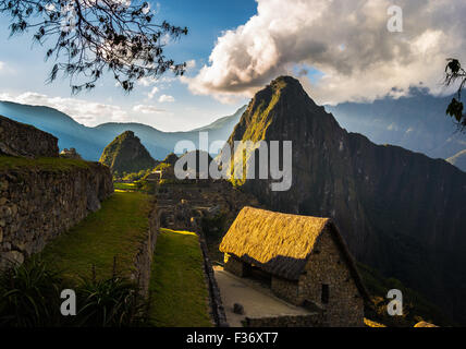 Machu Picchu parcialmente iluminada por los últimos rayos del sol. Amplio ángulo de visión de las terrazas con vistas panorámicas del cielo y resplandeciente de techo en t Foto de stock