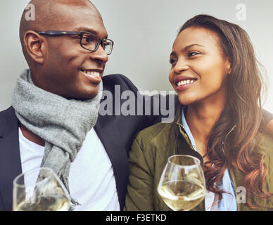 Romántica pareja joven afroamericano sentado disfrutando del brazo vasos de vino blanco y sonriendo amorosamente en cada uno de los demás e