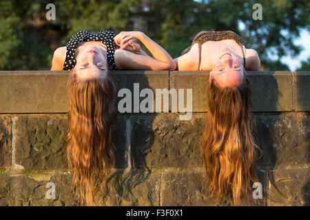 Dos niñas acostado sobre una losa de piedra con pelo largo colgando hacia abajo. Hermosa luz suave al atardecer. Foto de stock