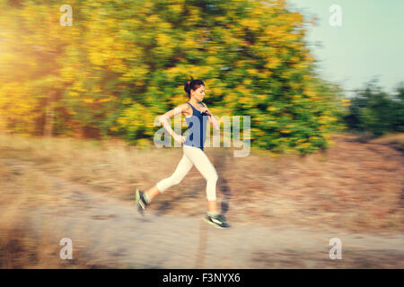 Mujer joven corriendo en un camino rural al atardecer en otoño del bosque. Antecedentes deportivos en el estilo de vida