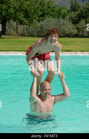 Adolescente de pie sobre los hombros de su padre en una piscina Foto de stock