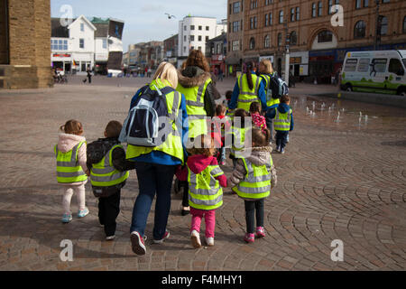 Protección primaria preescolar; niños con chaquetas protectoras fluorescentes de alta visibilidad en un paseo por Blackpool con cuidadores, Lancashire, Reino Unido
