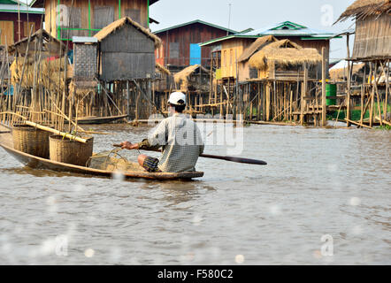 Las minorías étnicas fisheman Intha remando pequeña canoa tipo barco a lo largo de cursos de agua entre palafitos, Lago Inle, el Estado de Shan, Myanmar Foto de stock