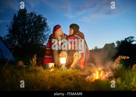 Camping joven pareja sentada por fogata al atardecer