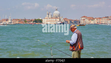 Hombre que pesca en la costa de Venecia con la Basílica di Santa Maria della Salute en el fondo Veneto Italia Europa