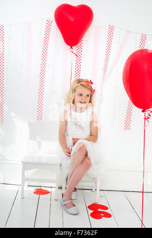 Chica posando para una foto en un estudio del fotógrafo, rodeado de globos rojos.