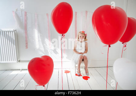 Chica posando para una foto en un estudio del fotógrafo, rodeado de globos rojos.