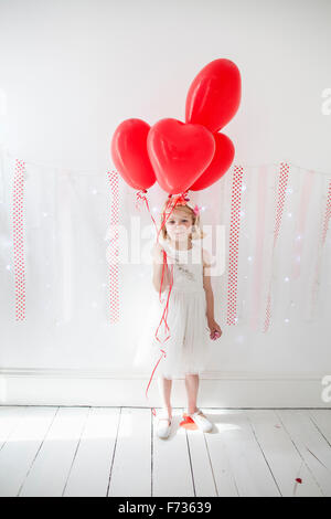 Chica posando para una foto en un estudio del fotógrafo, sosteniendo los globos rojos.
