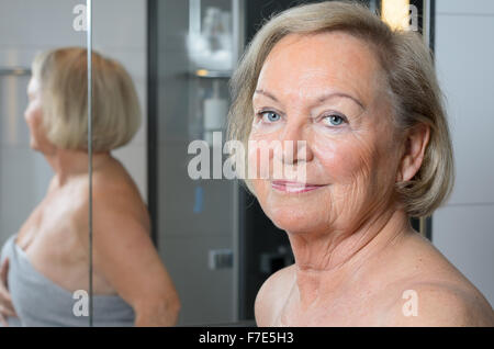 Mujer de pie senior rubia atractiva envuelta en una toalla de baño, cerrar un retrato de su cara con su cuerpo la reflexión Foto de stock