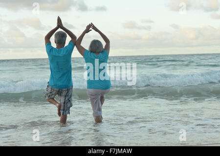 Pareja de ancianos hacer yoga en la playa Foto de stock