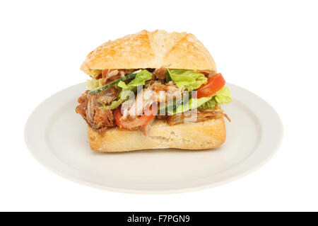 Carne de cerdo y ensalada en un bollo de pan de masa fermentada en una placa aislada contra un blanco Foto de stock