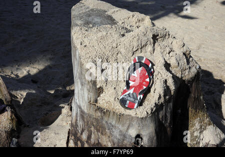 Una sola sandalia con un GB UK diseño bandera Union Jack encuentra reposando sobre un tocón de árbol cubierto de arena en la playa de Pattaya, Tailandia Foto de stock