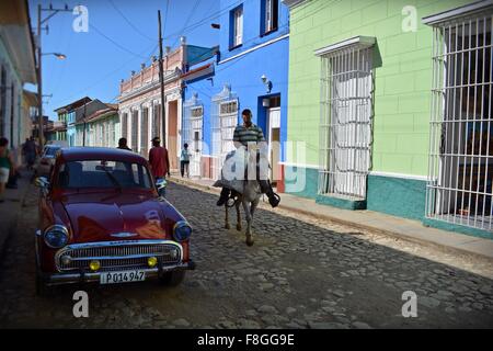 Jinete y peatones caminando por una calle adoquinada parcialmente sombreados en coloridos Trinidad provincia Sancti Spiritus Cuba