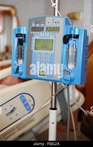 Bomba de infusión intravenosa por goteo IV junto a la cama en la habitación de un hospital. Foto de stock