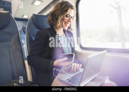 Mitad mujer adulta en el tren, utilizando smartphone y el ordenador portátil