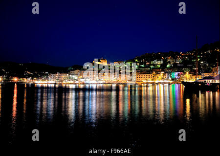 Panorama Night Shot, colorida iluminación de noche, con reflejo en el puerto de la ciudad de Porto Santo Stefano, en la costa de la Toscana, Italia Foto de stock