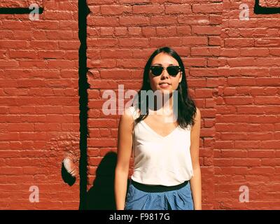 Retrato de joven y bella mujer de pie contra la pared de ladrillo rojo