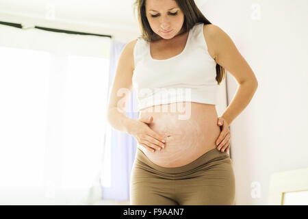 Hermosa mujer embarazada aplicar anti humectante o crema de la marca del estiramiento