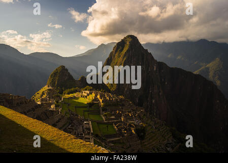 Machu Picchu parcialmente iluminada por los últimos rayos del sol. Amplio ángulo de visión de las terrazas con vistas panorámicas del cielo y el sendero brillante Foto de stock