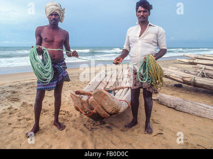 Dos pescadores indios permanecer juntos por su barco hecho crudo de registros y sujetar la cuerda en sus manos hacia adelante en la playa