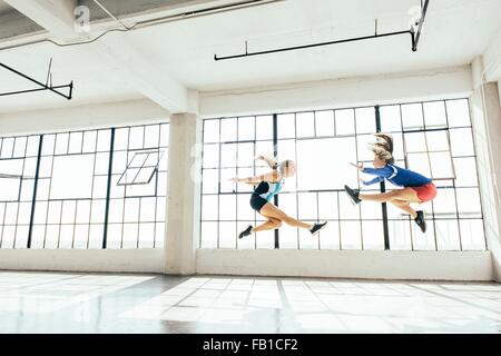 Vista lateral de ángulo bajo de mujeres jóvenes en el gimnasio haciendo lunge con aire. Foto de stock