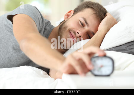 Feliz despertar de un hombre feliz tumbado en la cama y Detener reloj alarma Foto de stock
