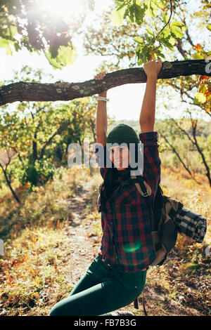 Retrato de mujer sonriente balanceándose de rama en el bosque Foto de stock