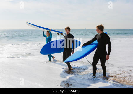 Portugal, Lisboa, tres personas llevar tablas de surf en la playa