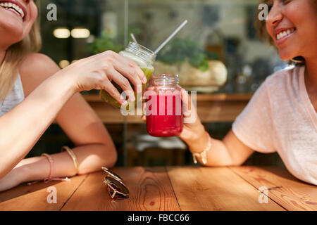 Primer plano de amigas jugo tostado gafas al café en la acera. Dos mujeres felices disfrutando de bebidas frescas en el café al aire libre