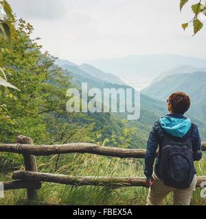 Vista trasera del hombre con mochila estando en contra de las montañas