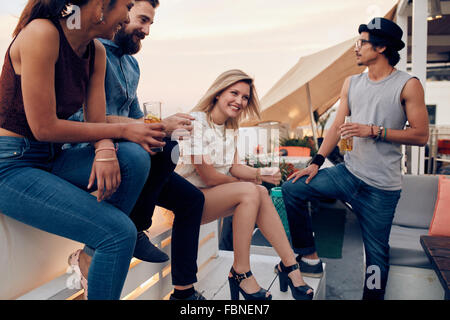 Un grupo de amigos, colgada en un tejado con bebidas. Los jóvenes de fiesta junto con cócteles. Foto de stock