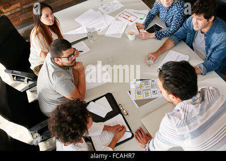 Un alto ángulo de visualización del equipo creativo sentados en torno a una mesa discutiendo ideas de negocio. Raza mixta, equipo de profesionales creativos meeti Foto de stock