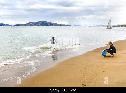 Vista de un surfista en su tabla de surf traje húmedo o skimboarding en aguas poco profundas en la Bahía de San Francisco, en la costa de playa, sa Foto de stock