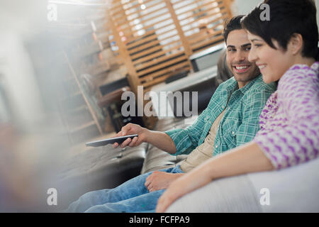 Una pareja, hombre y mujer sentada en un sofá en casa, uno sosteniendo un dispositivo de control remoto.