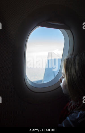 Niña mirando por la ventana del avión mientras avión está volando.