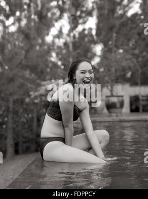 Una mujer se sienta en la cornisa de la piscina infinity en la Granja de San Benito, Filipinas. Foto de stock