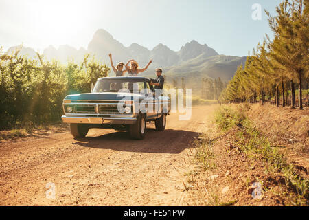 Amigos divirtiéndose en la abertura de la parte trasera de un camión vintage en un día de verano en el campo. Los jóvenes hombres y mujeres disfrutando de una carretera tr