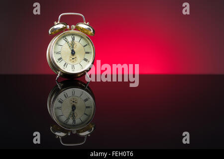 Vintage despertador mostrando cinco minutos a doce, fondo rojo, espacio de copia Foto de stock
