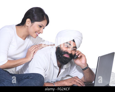 Sikh hombre hablando por teléfono móvil con un ordenador portátil y una mujer mirando la pantalla MR#702Z;779A Foto de stock