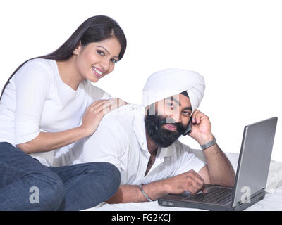 Sikh hombre hablando por teléfono móvil con el portátil y la mujer señor#702Z;779A Foto de stock
