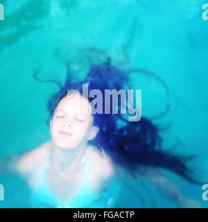 Un alto ángulo de visualización de la mujer joven con los ojos cerrados en la piscina