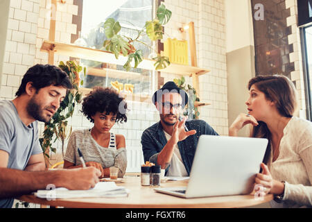Retrato de negocio creativo equipo sentado en una cafetería con un portátil. Joven para debatir nuevas ideas de negocio con los colegas