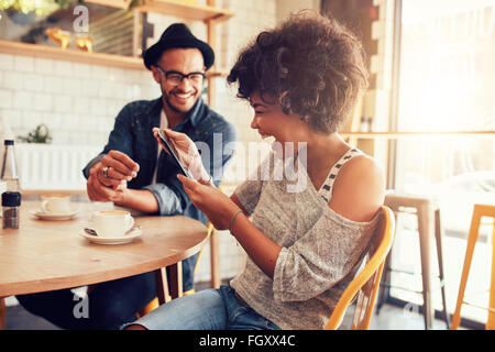 Retrato de mujer sonriente en una mesita de café mirando tableta digital con un amigo sentado.