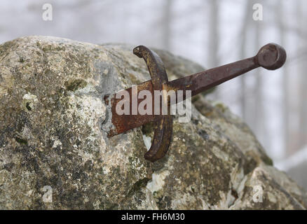 La legendaria espada Excalibur en la piedra en el medio del bosque en invierno Foto de stock