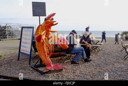 Un par comer mariscos en uno de los tenderetes en Brighton Seafront UK junto a una gigantesca langosta de plástico Foto de stock