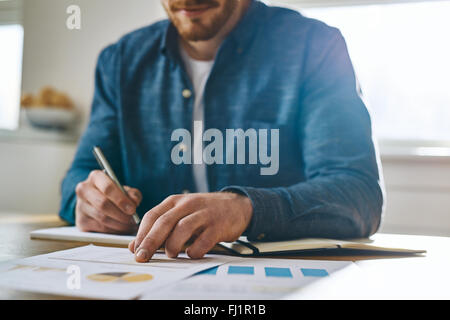 Vista focalizada de inidentificables Hombre con camisa azul con la mano sobre el papeleo, como si para comprobar notas o comparar la información
