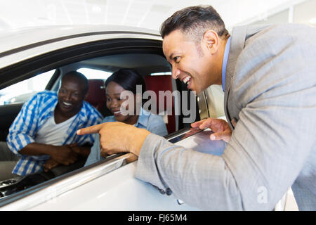 Vehículo de mediana edad vendedor mostrando nuevo coche a una joven pareja en showroom Foto de stock