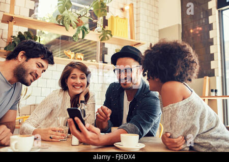 Retrato de un grupo de jóvenes amigos en un café y mirar las fotos en el teléfono móvil. Hombres y mujeres jóvenes sentados en