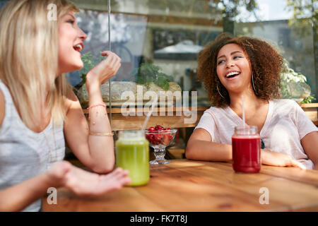 Dos mujeres chismeando y sonriente en un restaurante. Jóvenes amigos sentado en la cafetería al aire libre para divertirse.