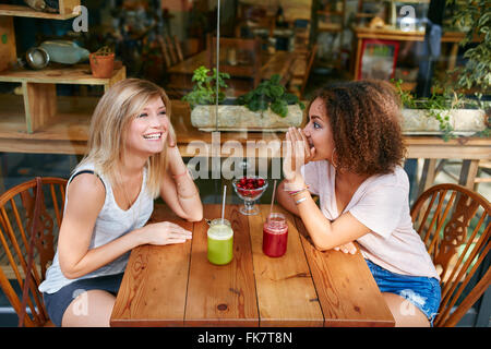 Las hembras jóvenes amigos que chismorrea privado en café en la acera. Dos jóvenes mujeres chismeando y susurrando en una cafetería al aire libre